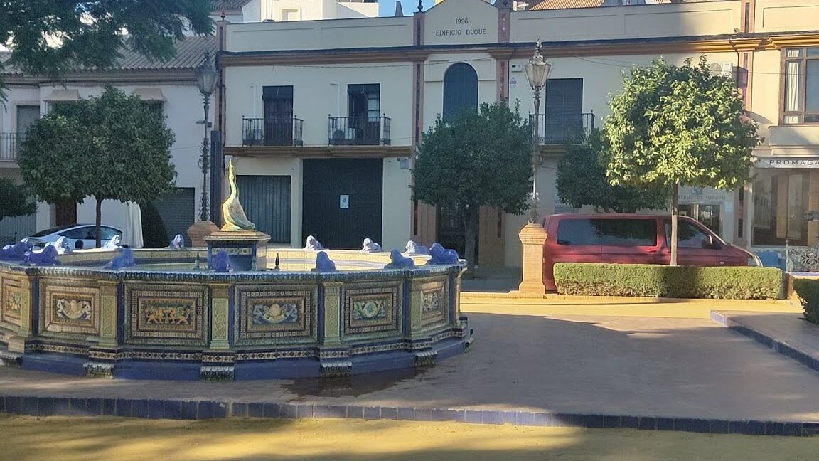Fuente cerámica octogonal en plaza con árboles y fachadas, sugerente escenario para el Mercado Navideño de Alcalá de Guadaíra.