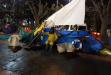 Puesto decorado con velero y vendedor con chubasquero amarillo en la plaza del Mercau Agroecoloxicu y Artesanu de la Montaña Central