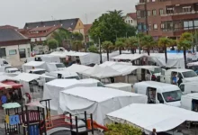Mercado de Antigüedades Noja Vintage con puestos y furgonetas bajo toldos en una plaza lluviosa