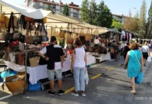 Visitantes recorriendo puestos al aire libre en la Feria Desembalaje de Antigüedades de Torrelavega con bolsos y ropa en exposición.