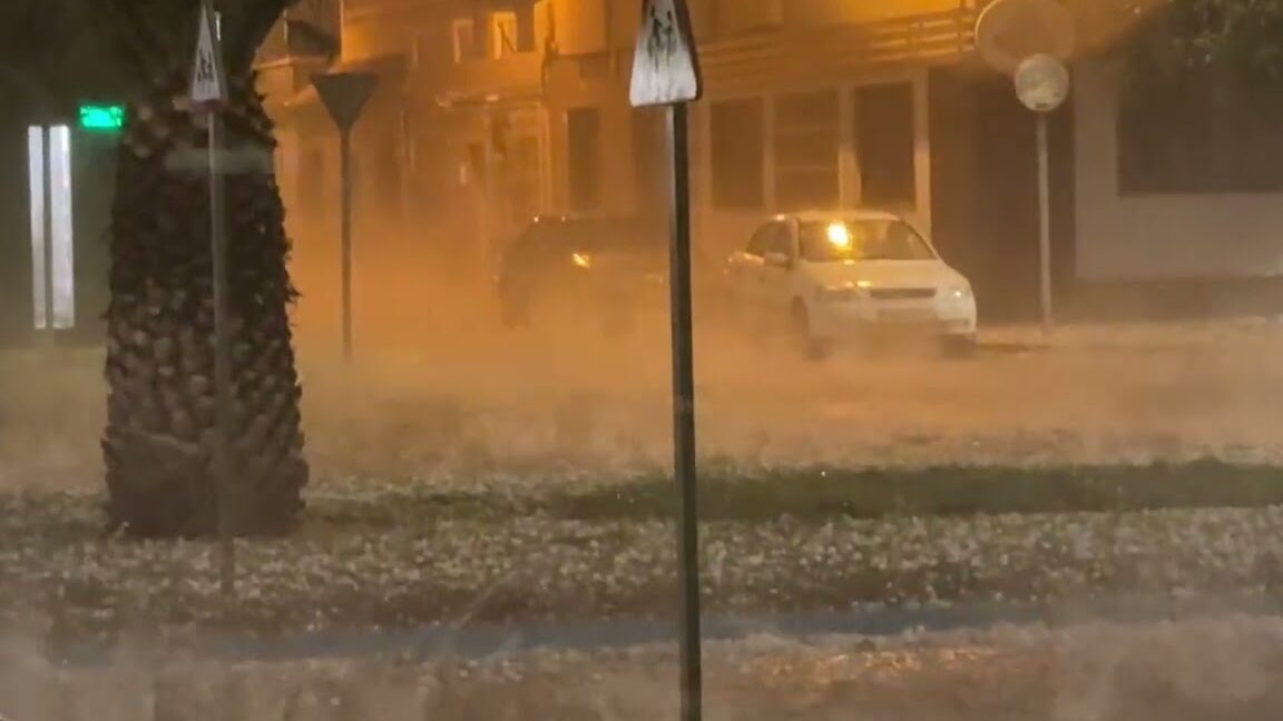 Calle nocturna con granizo y agua acumulada frente a coches y farolas, Mercado Navideño de El Ejido