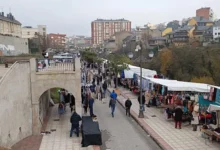 Mercadillo de Antigüedades de Ponferrada con filas de puestos cubiertos y personas paseando por un paseo junto al río