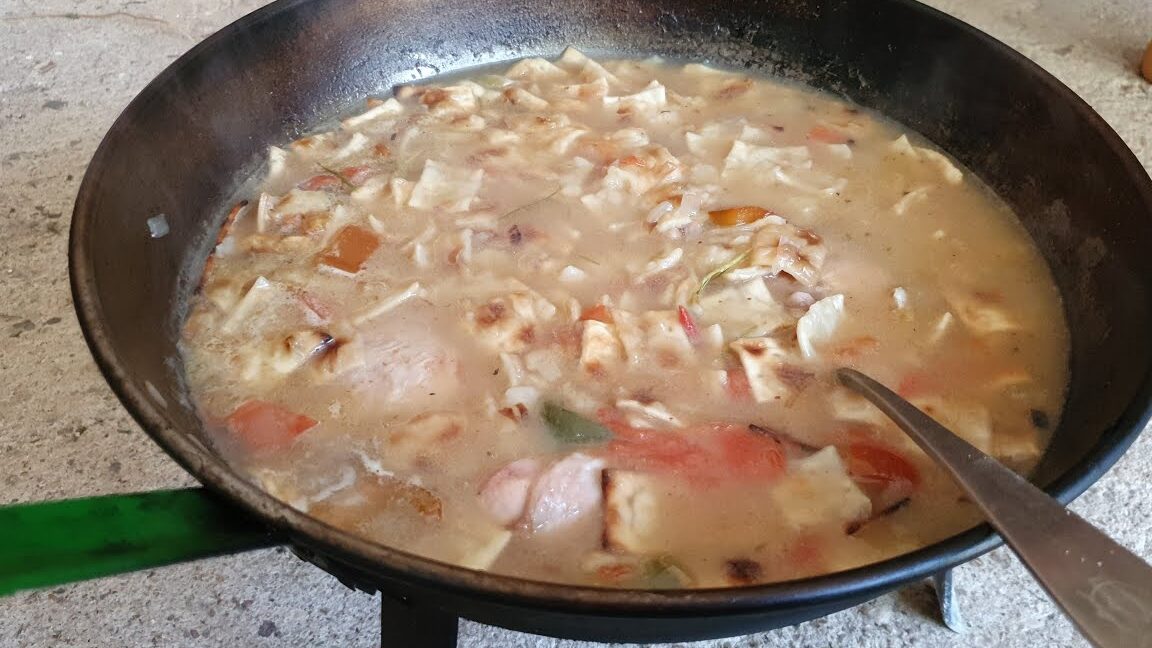 Guiso espeso con trozos de verdura y carne en paellera sobre hornillo, Mercadillo de Cascaruja y Porrate de Navidad