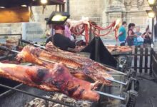 Mercadillo de Antigüedades de El Puerto de Santa María con asadores de cochinillo, embutidos colgados y puestos en plaza histórica.