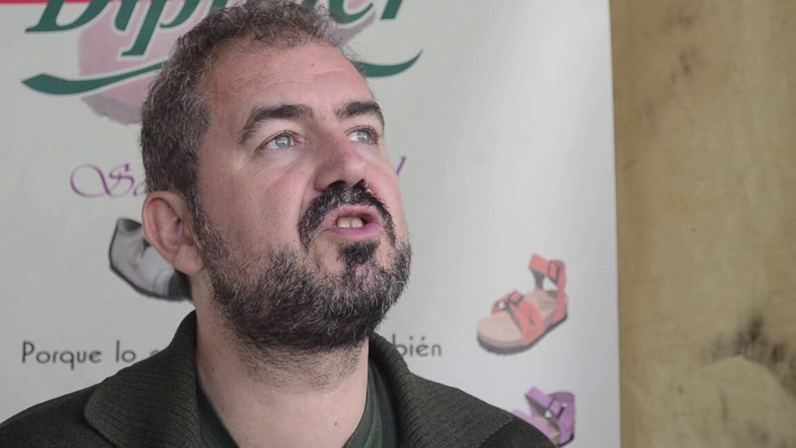 Hombre con barba hablando frente a un cartel promocional en el Mercado Ecológico de Cuéllar