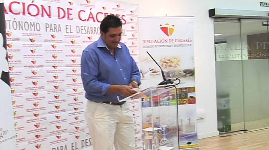 Orador junto a un atril durante la presentación del Mercado Ecológico de Palazuelos de Eresma con fondo de la Diputación de Cáceres