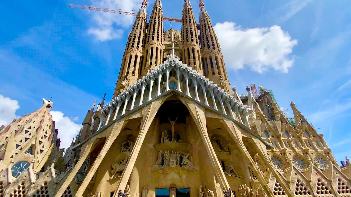 Feria de Navidad de la Sagrada Familia frente a la fachada detallada de la basílica de la Sagrada Familia bajo un cielo azul