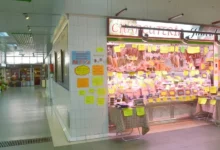Puesto de charcutería con embutidos colgados y múltiples etiquetas de precios en un pasillo de mercado, Mercado Ecológico de Segovia.