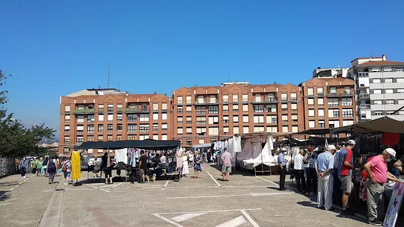 Mercado de Aldeanas de Portugalete con puestos al aire libre, ropa colgada y compradores paseando bajo un cielo azul